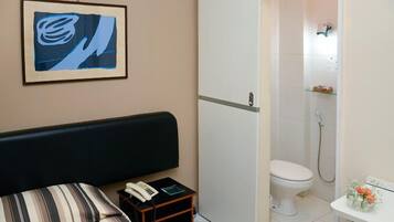 A hotel room with a bed, a bedside table with a phone, a framed artwork, a toilet, and a shower area.