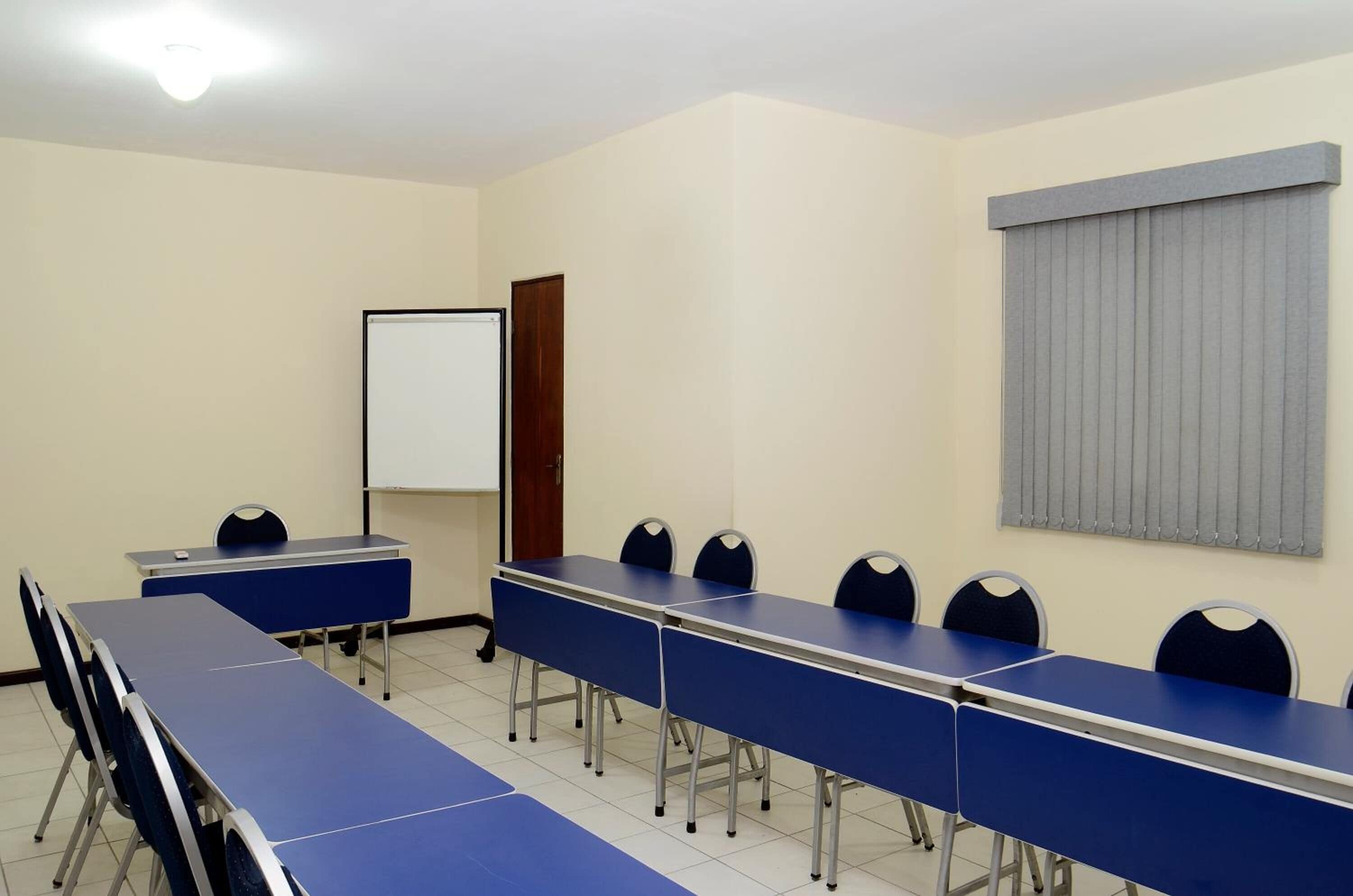Un salón de conferencias con una larga mesa, sillas, una pizarra y una ventana con persianas.
