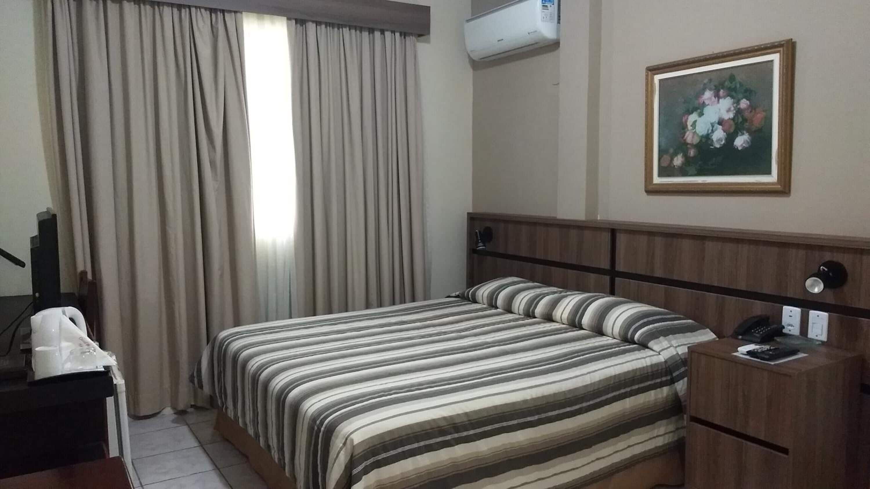 A hotel room with a bed, a desk, a telephone, and a painting on the wall.