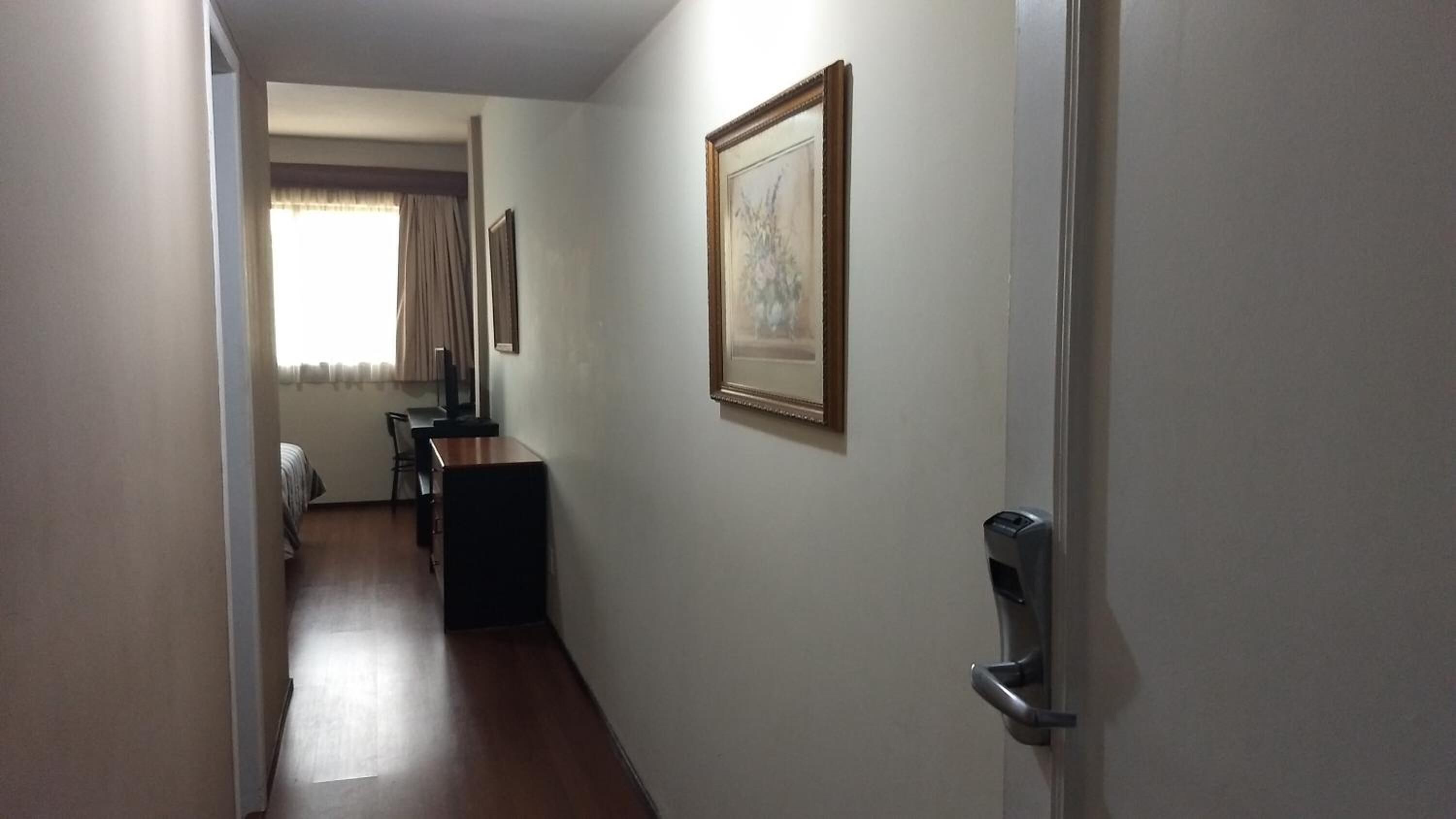 A narrow hallway with a desk and chair, a bed, and a door with a handle.