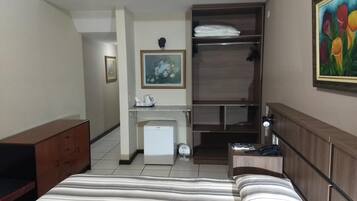 Une chambre d’hôtel comprenant un lit, un bureau avec une chaise, un petit réfrigérateur, une armoire et un tableau au mur.