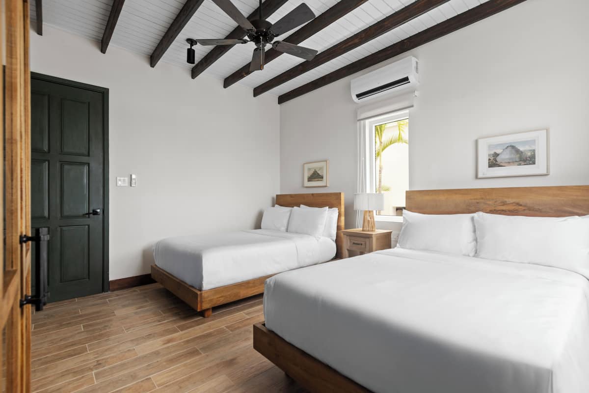 A hotel room with two beds, wooden headboards, a ceiling fan, and a window with a view.