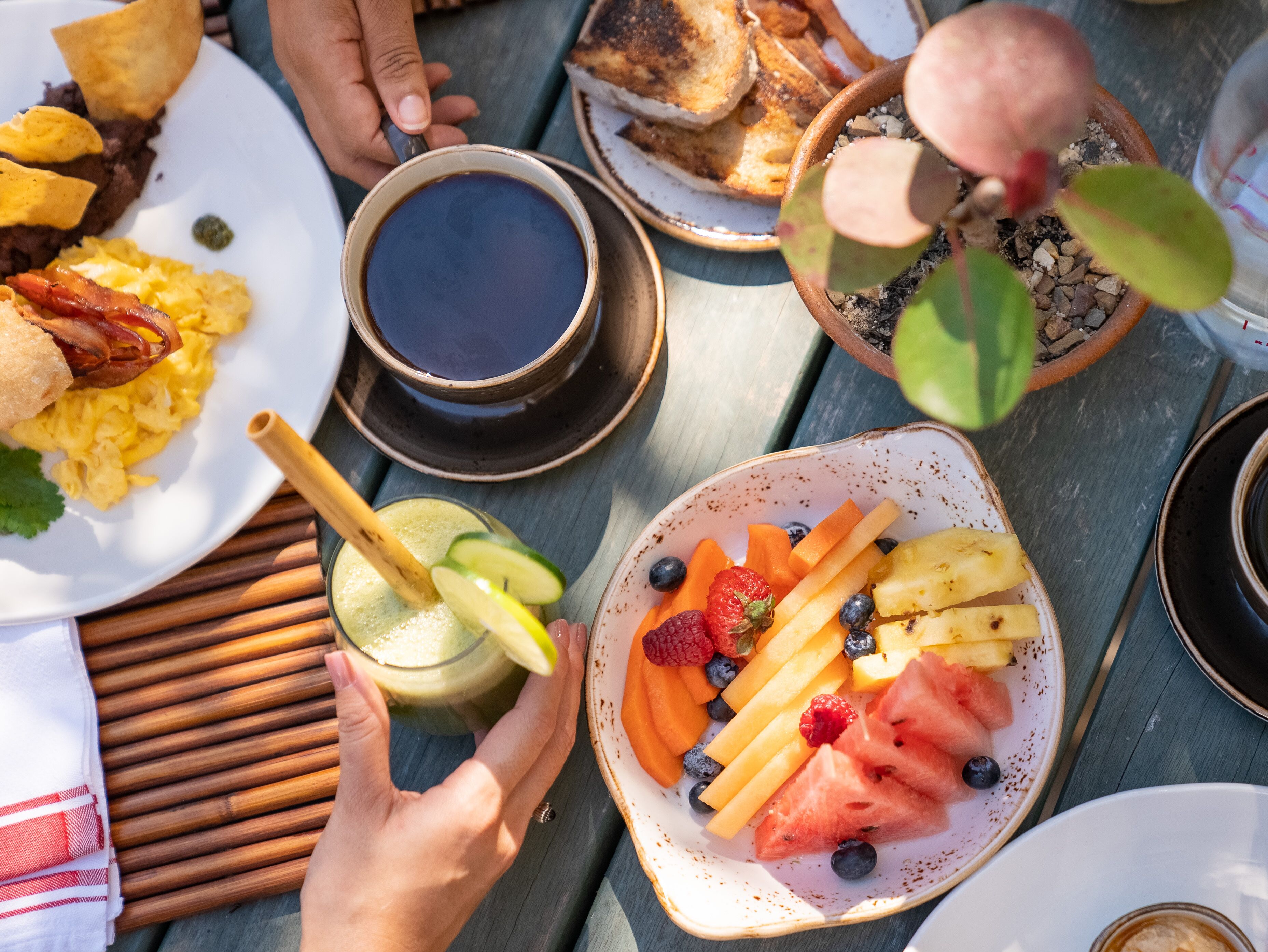 A breakfast setting with various food items and a cup of coffee on a wooden table.