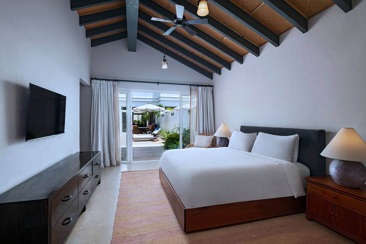 A modern hotel room with a large bed, a TV, a wooden ceiling, and a view of the outdoor area.