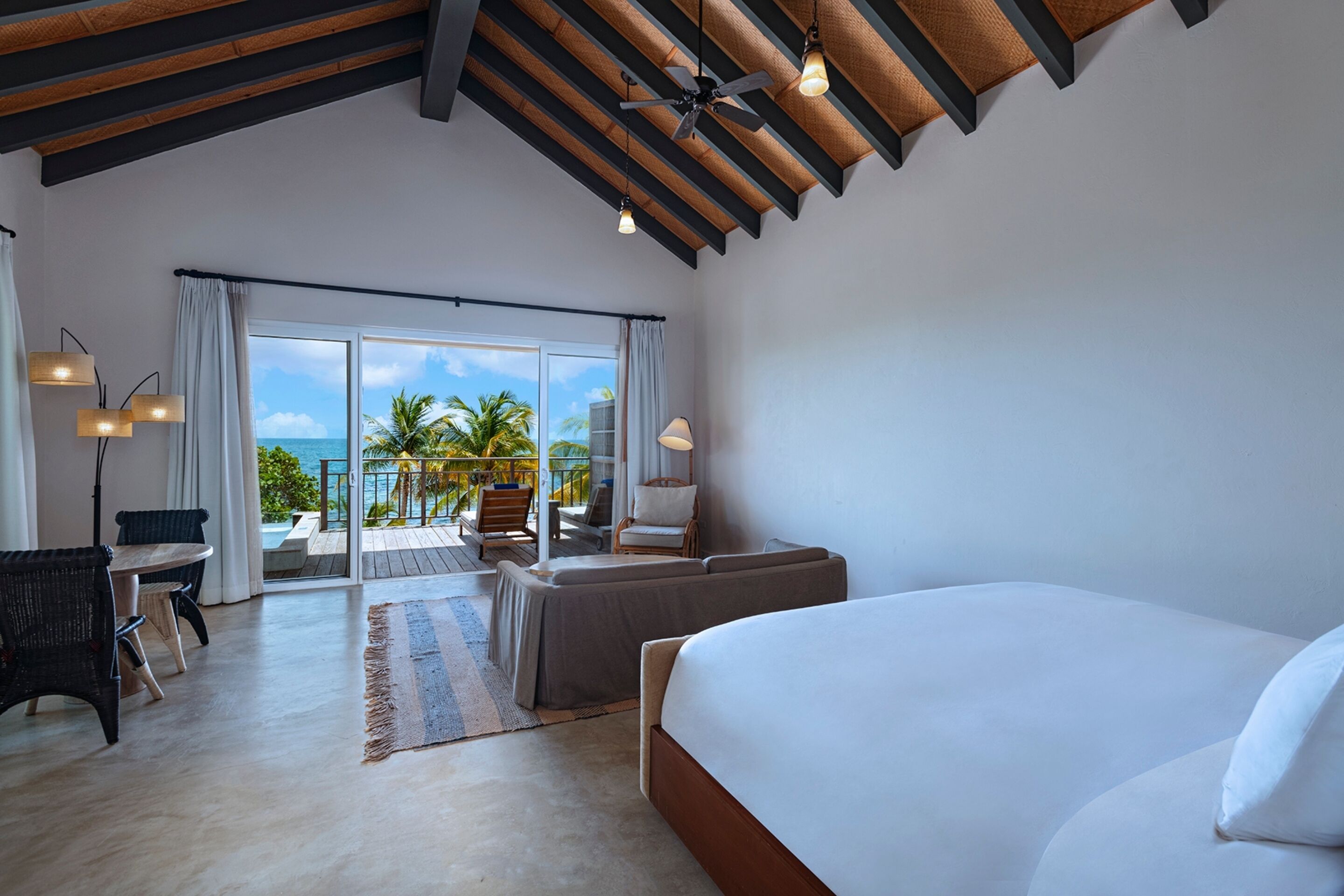 A spacious bedroom with a large bed, a balcony with a view of the ocean, and a ceiling fan.