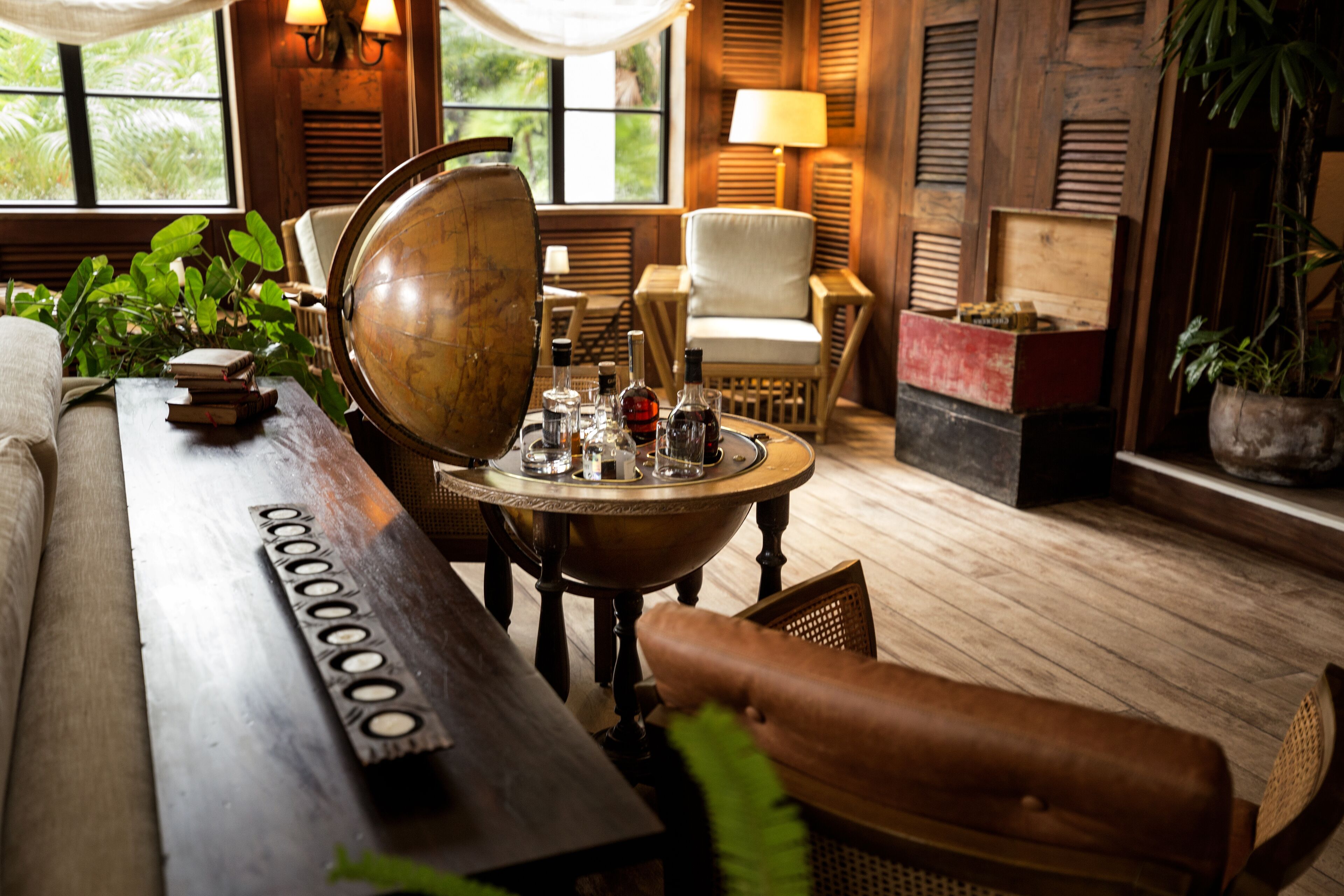 A cozy room with a wooden floor, a globe, a table with bottles, a sofa, and a chair.