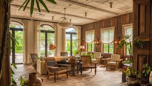 A spacious room with wooden flooring, large windows, and a variety of seating arrangements including chairs and a sofa. - Itz'ana Resort & Residences (Placencia)