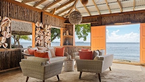 A beachside room with wicker furniture, a thatched ceiling, and a view of the sea. - Itz'ana Resort & Residences (Placencia)