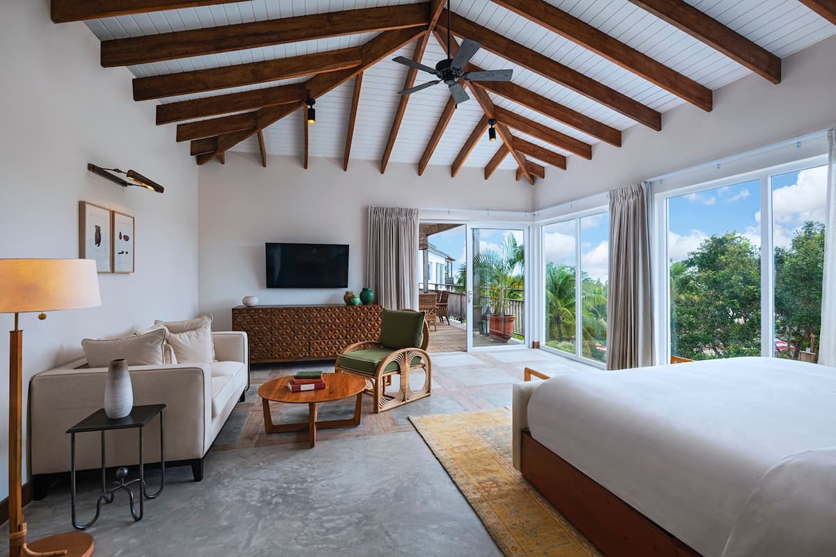 A spacious room with a large bed, a sofa, a television, and a balcony with a view of the outdoors.