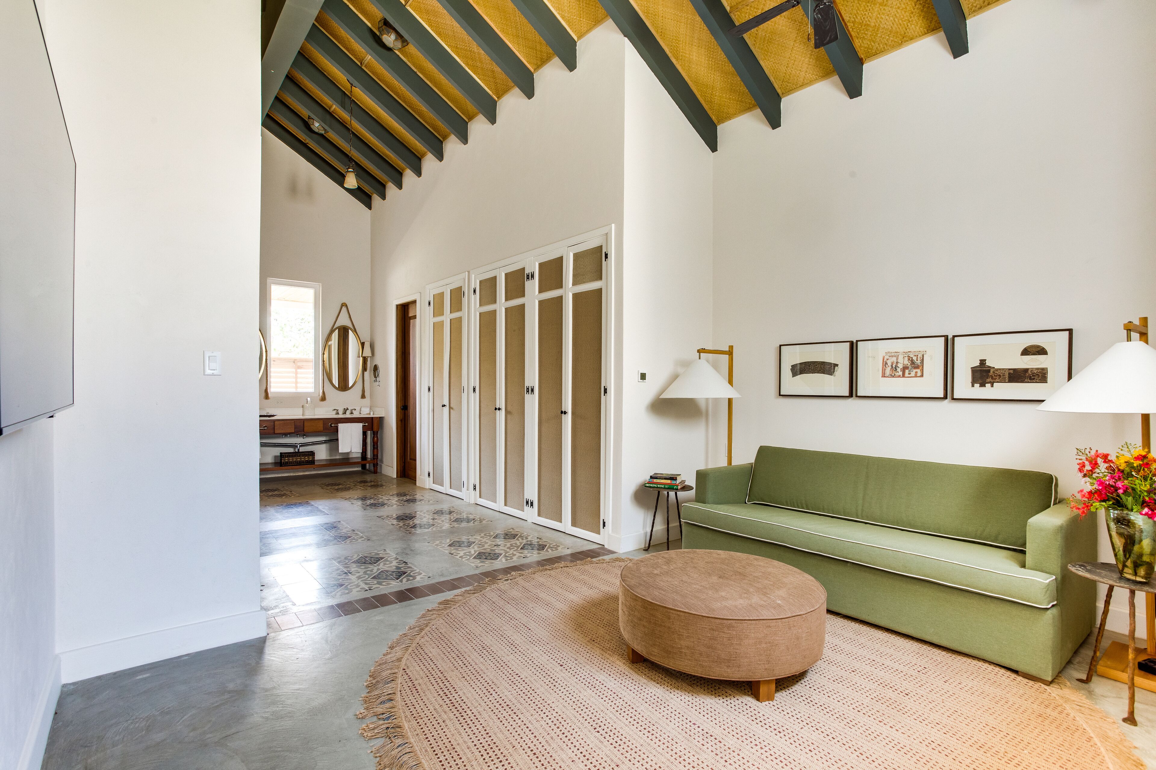 A spacious living room with a green sofa, a round ottoman, and a woven rug.