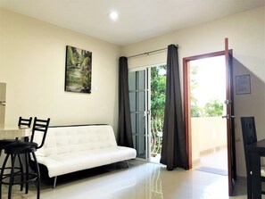 A modern living room with a white sofa, black chairs, a dining table, and a large window with curtains.