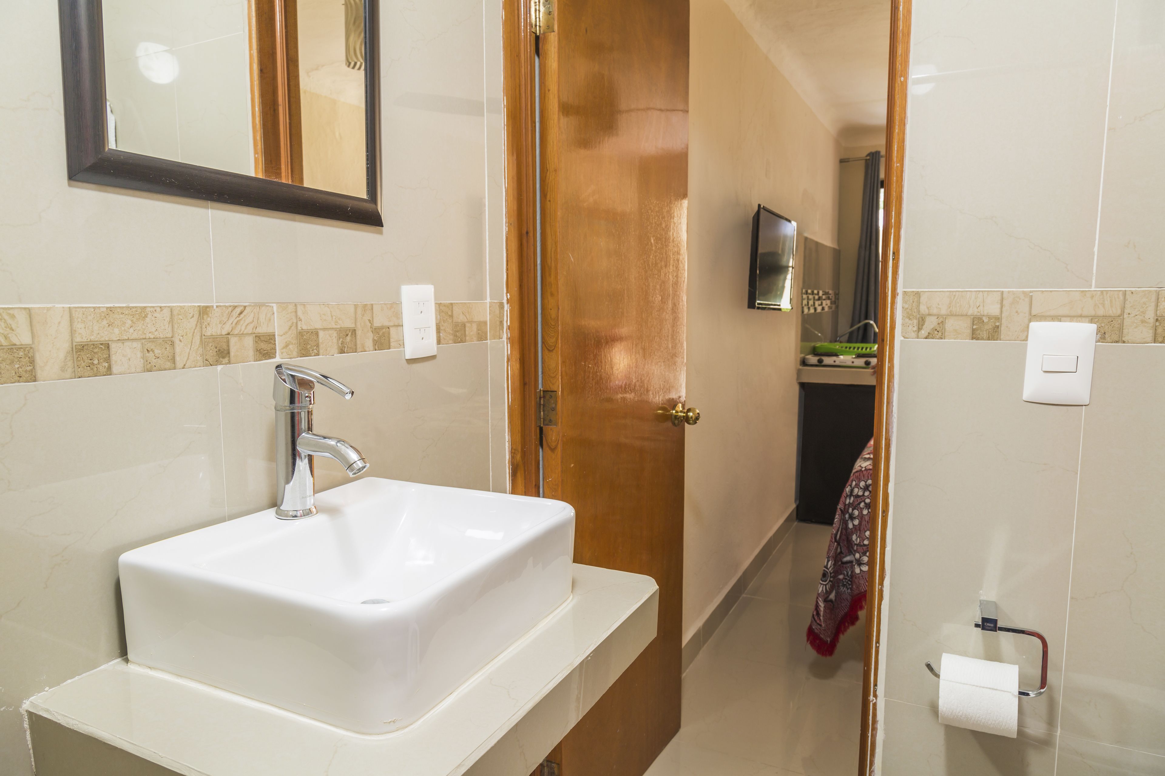 A bathroom with a white sink, a mirror, and a door leading to another room.