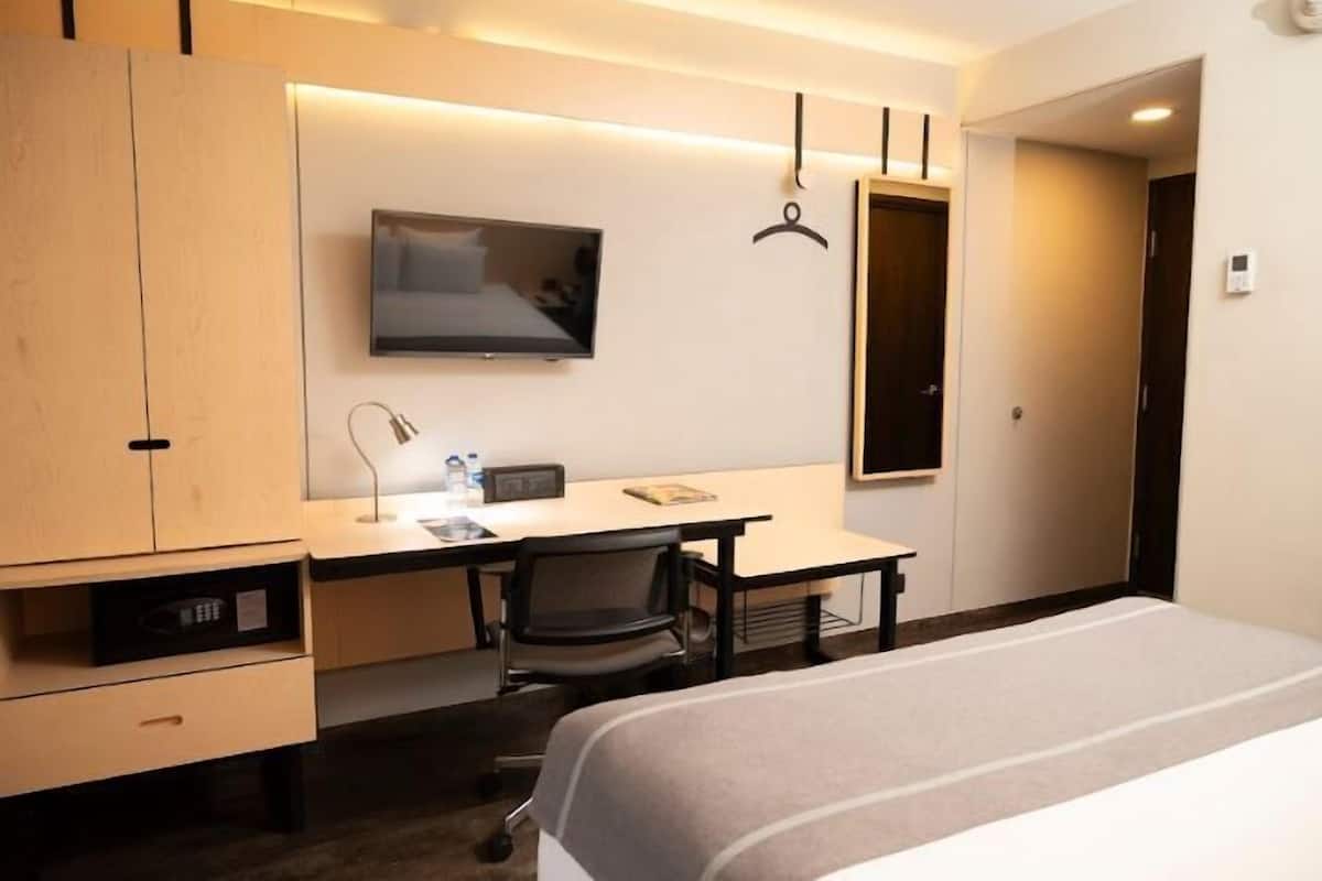 A hotel room with a bed, a desk, a chair, a television, and a wardrobe.