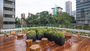 Een terras op het dak met houten meubels, planten in potten en uitzicht over de stad.