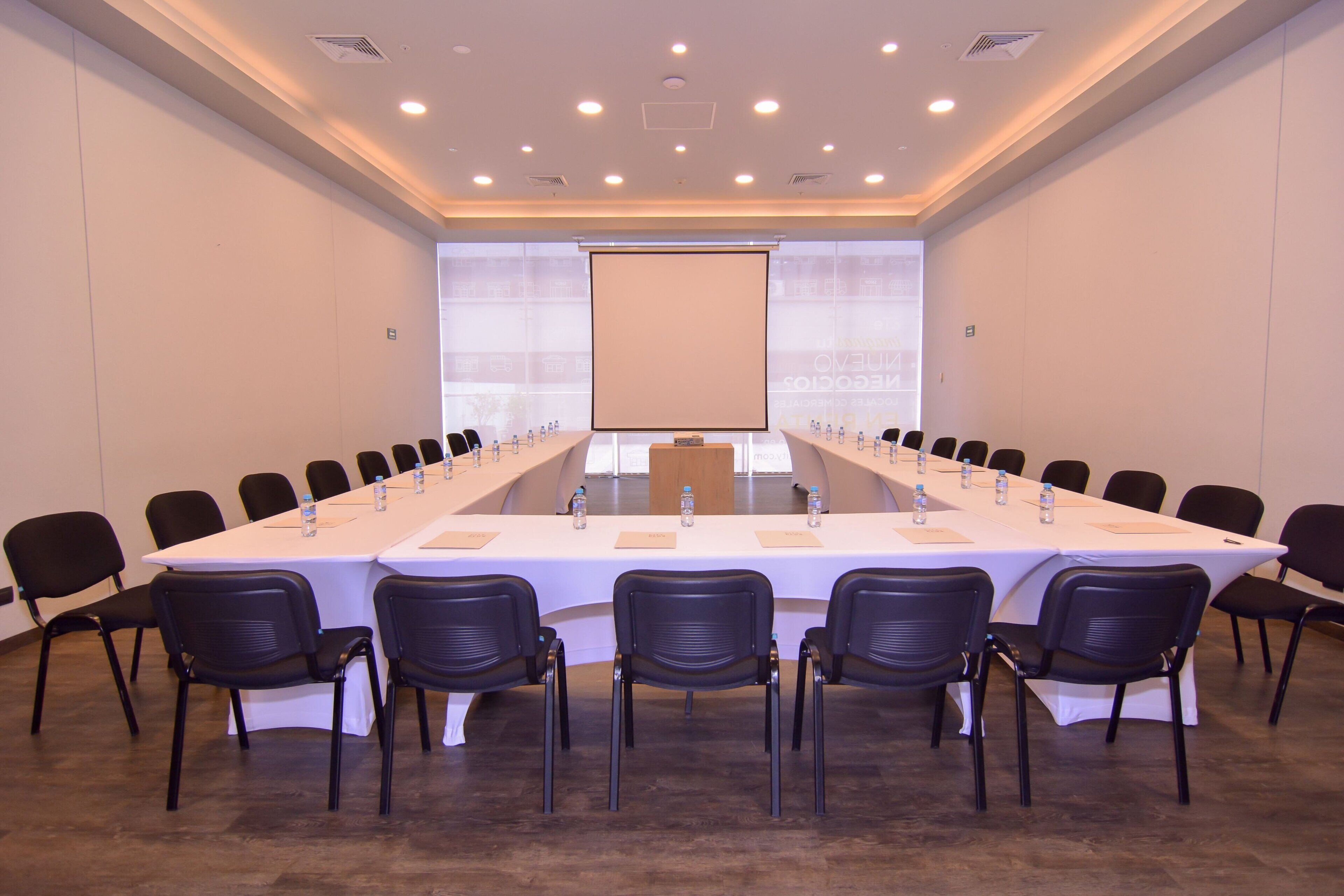 Ein Konferenzraum mit einem langen Tisch, Stühlen und einer Projektionsleinwand.