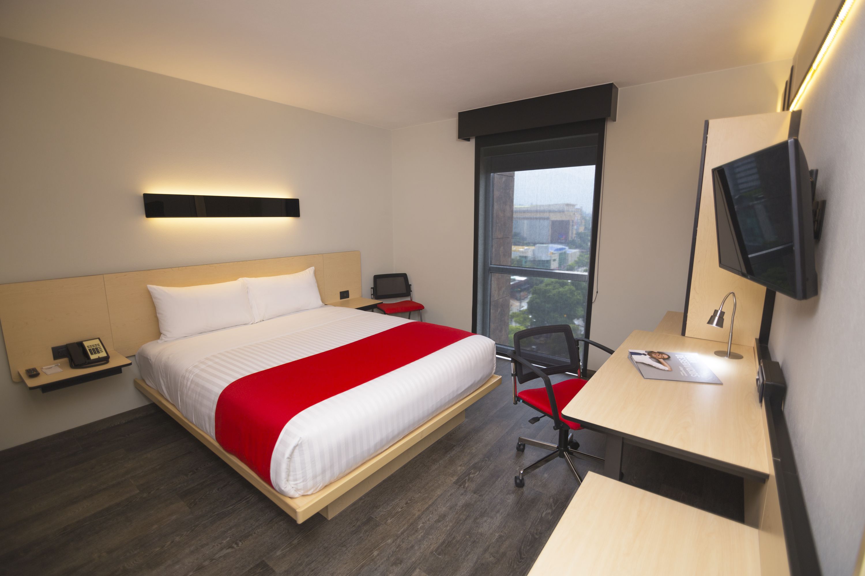 A hotel room with a bed, bedside tables, a desk, a chair, a TV, and a window with a view.