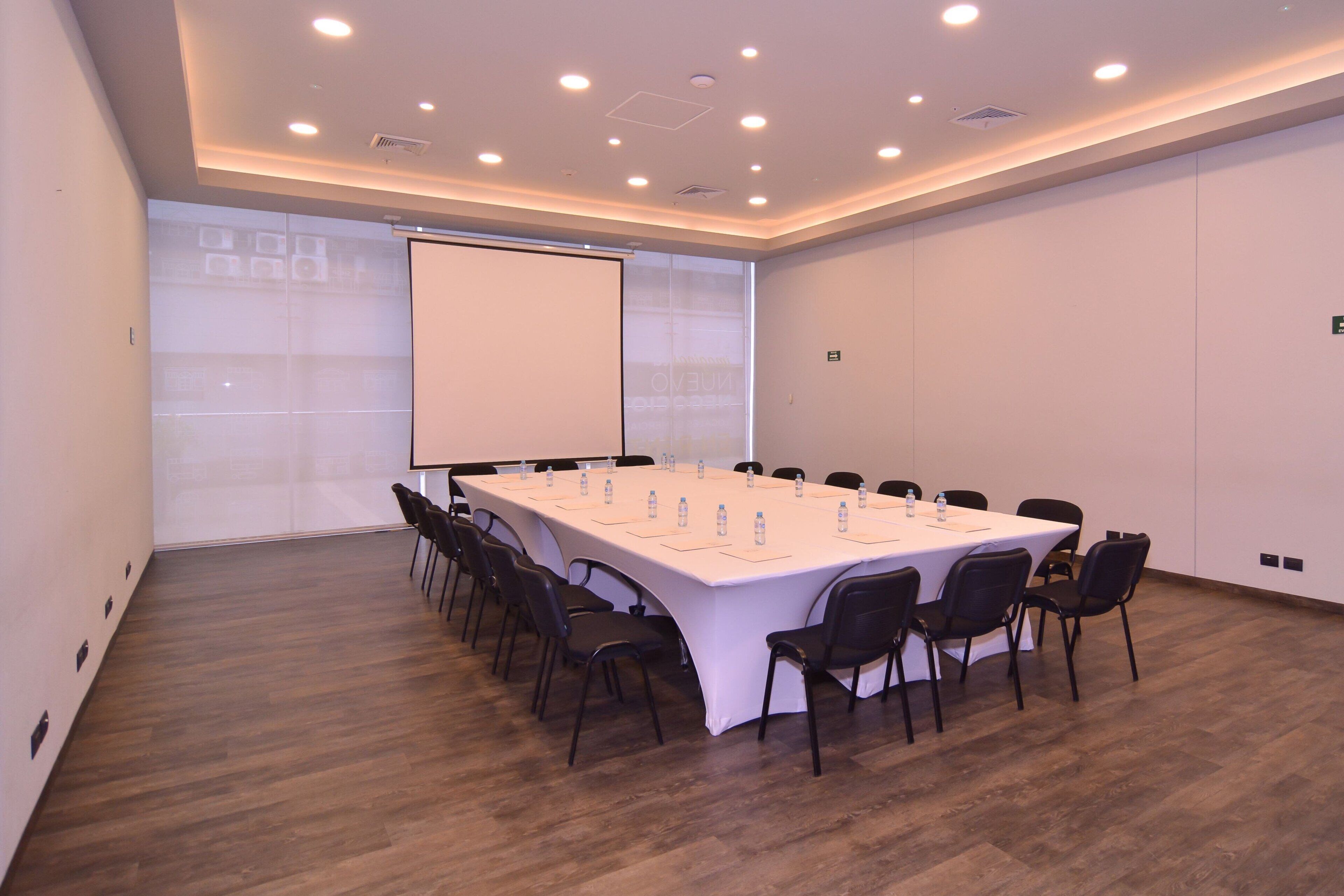 Una sala de conferencias con una larga mesa, sillas, una pantalla de proyector y una pizarra.