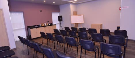 Un salón de conferencias con filas de sillas, un atril, una pizarra blanca y un altavoz sobre un trípode.