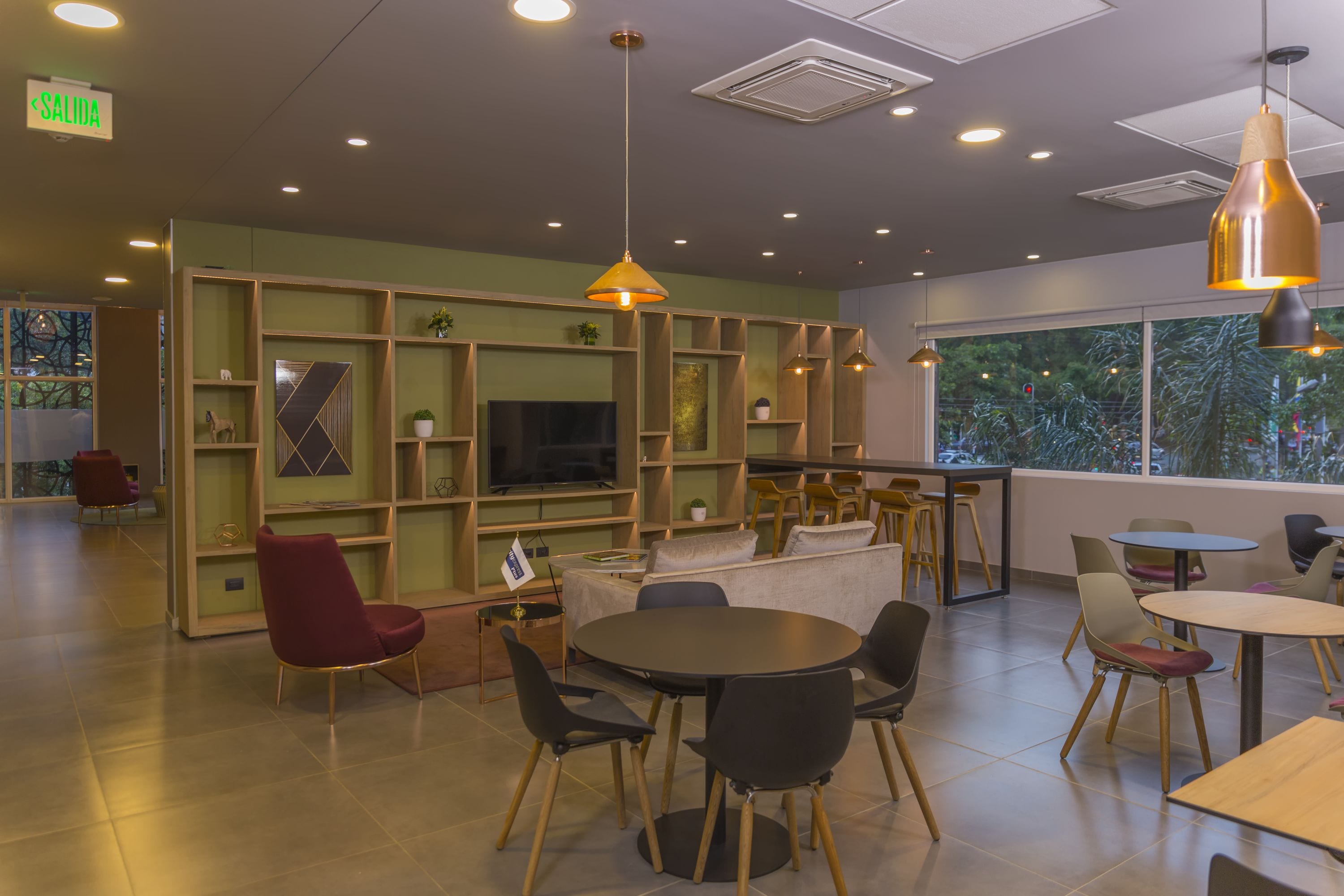 A modern interior with a green wall, wooden shelves, a TV, and a mix of seating arrangements including chairs and tables.