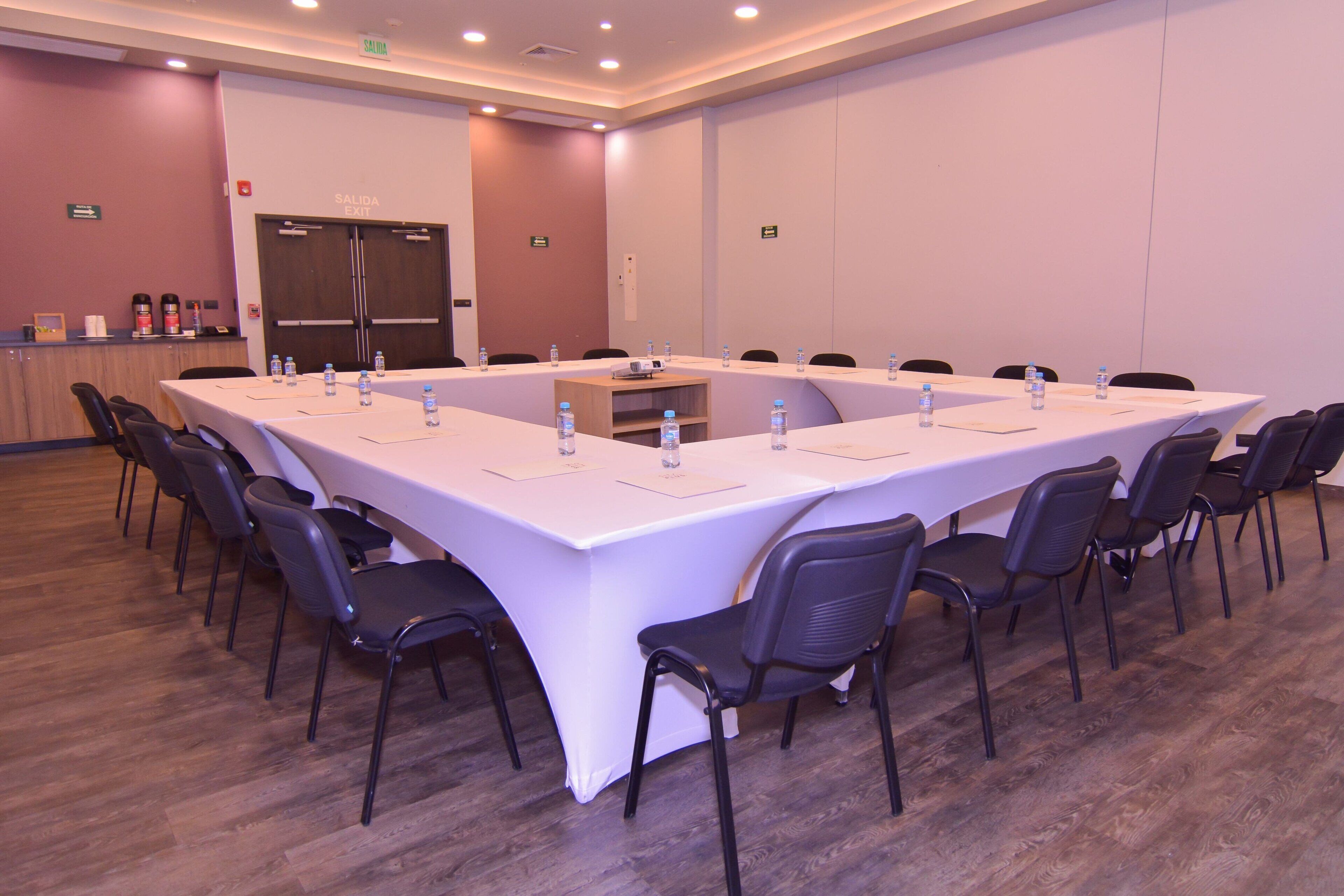 A conference room with a long table, chairs, water bottles, and a projector.