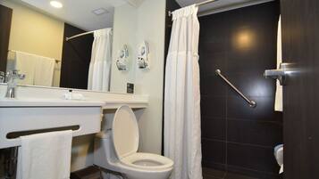 Un baño moderno con inodoro blanco, lavamanos con espejo y zona de ducha con cortina.