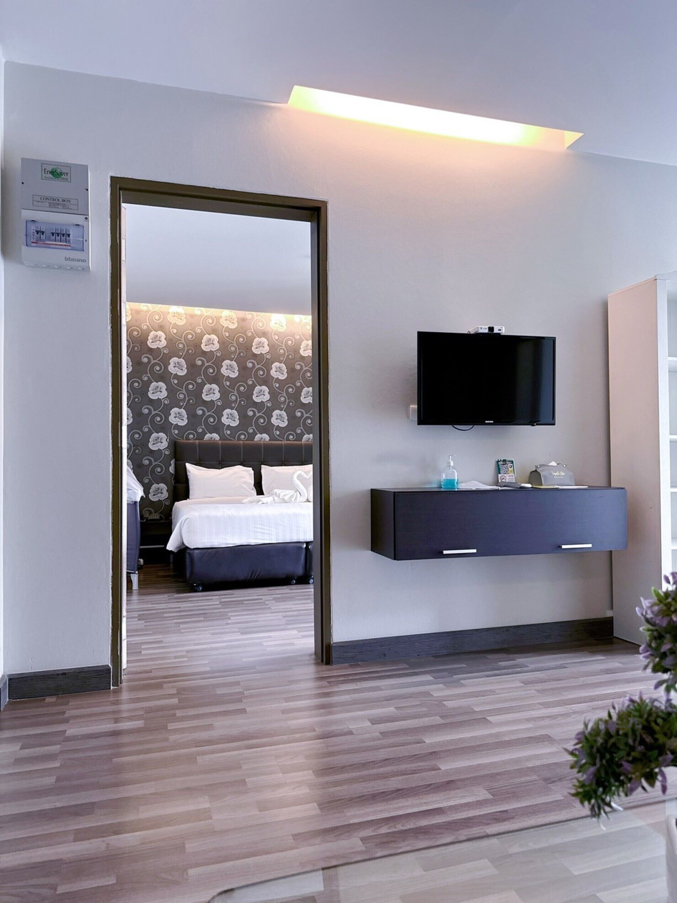 A modern hotel room with a bed, a TV mounted on the wall, and a bedside table with a lamp and a small plant.