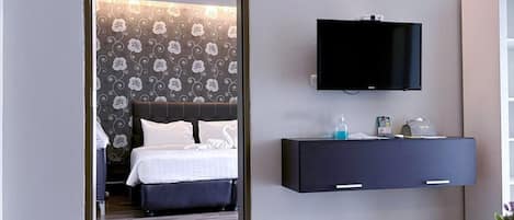 A modern hotel room with a bed, a TV mounted on the wall, and a bedside table with a lamp and a small plant.