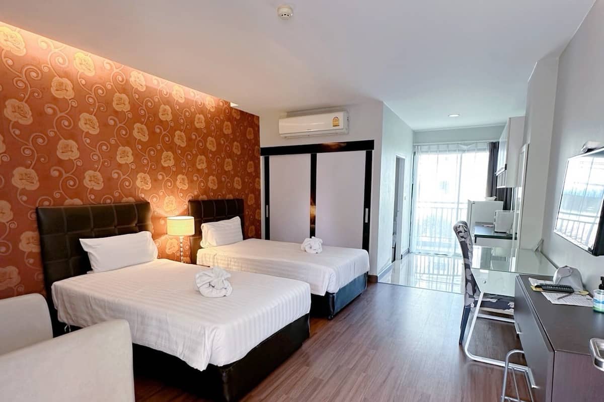 A hotel room with two beds, a desk, and a chair. There is a window with a view of the outside.
