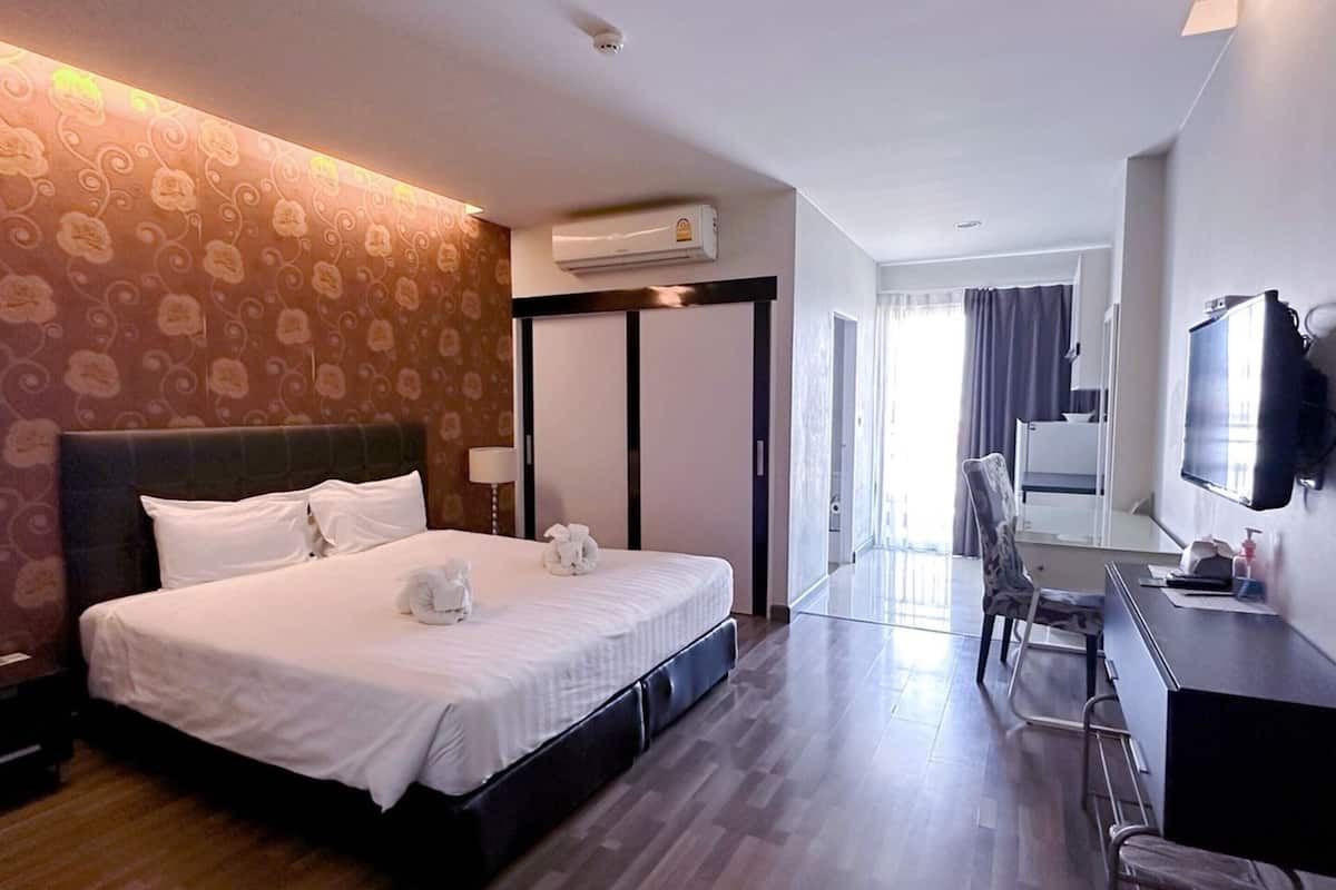 A hotel room with a large bed, a desk, a chair, and an air conditioning unit.