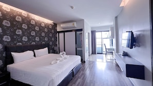 A modern hotel room with a large bed, a flat-screen TV mounted on the wall, and a view of the outdoors through a sliding door. - Romyen Garden Place (Nakhon Ratchasima)