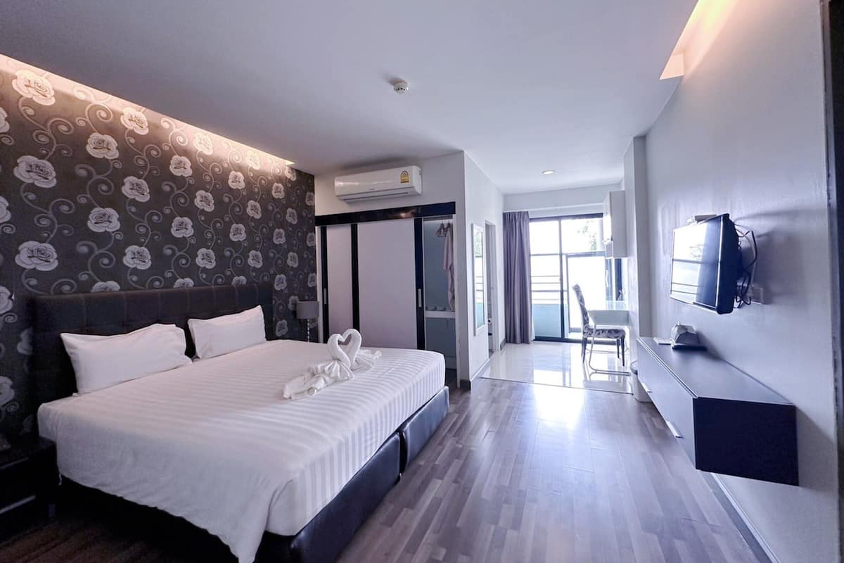 A modern hotel room with a large bed, a flat-screen TV mounted on the wall, and a view of the outdoors through a sliding door.