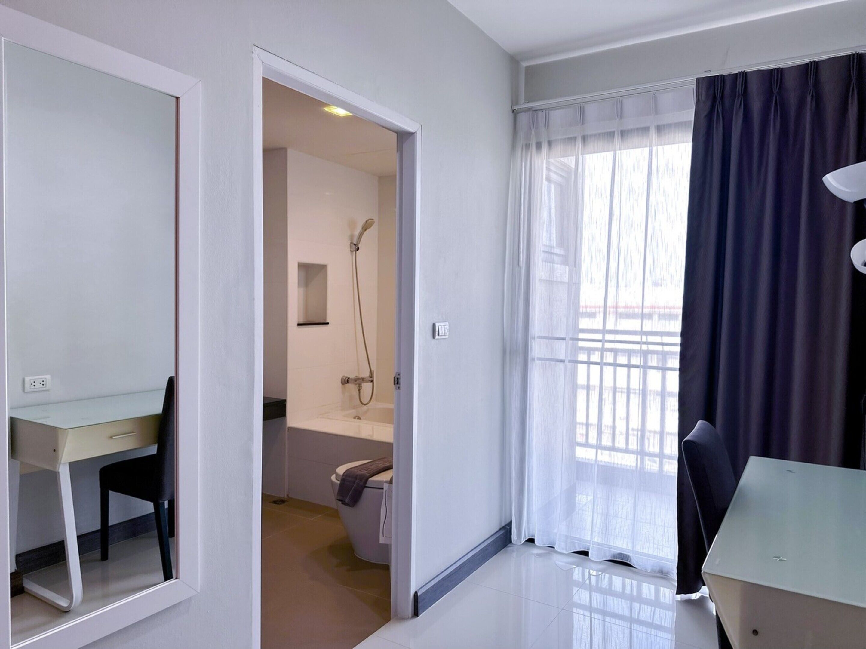 A modern hotel room with a desk, chair, and a view of a balcony with curtains.