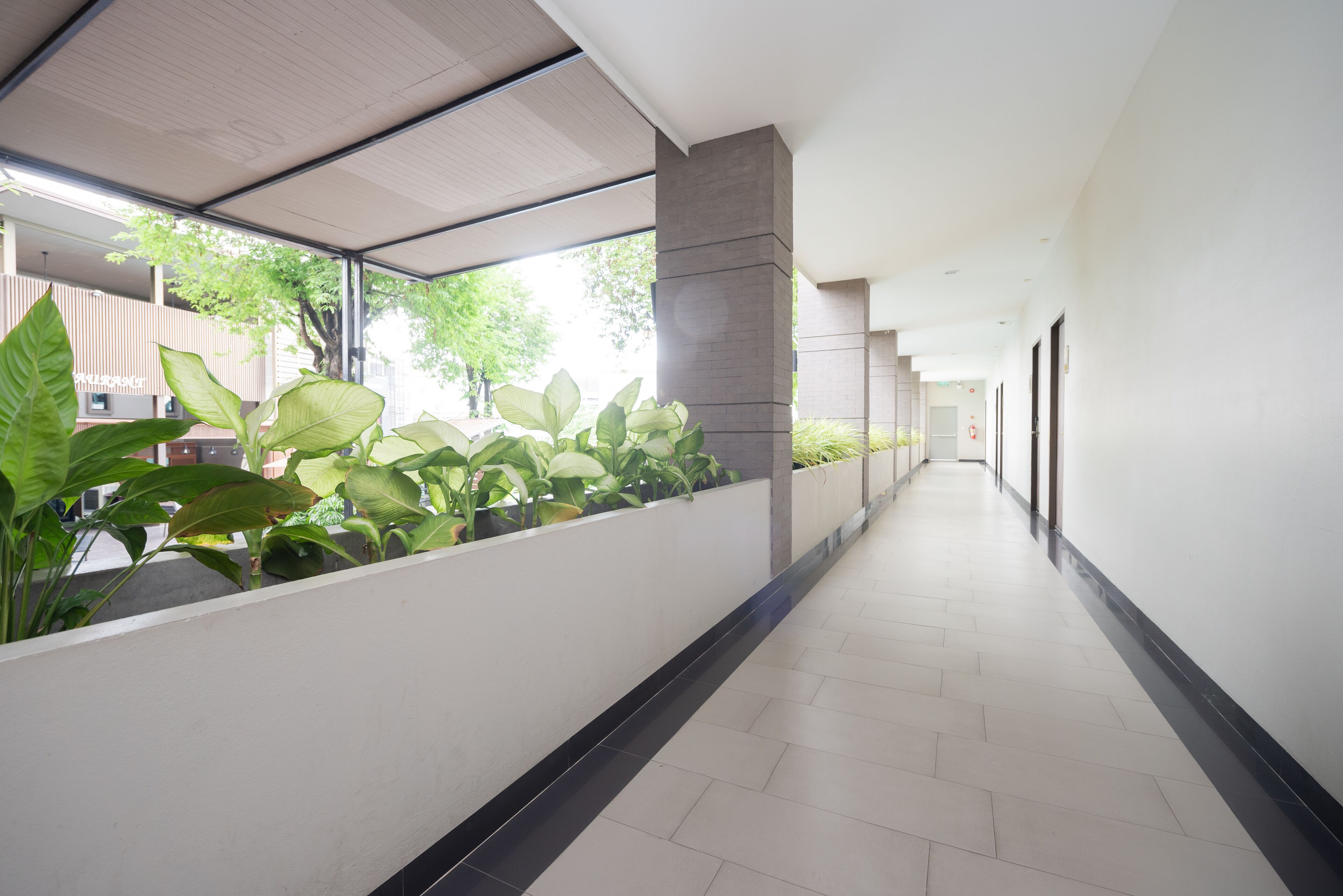 A corridor with a tiled floor, a planter with green plants, and a modern architectural design.