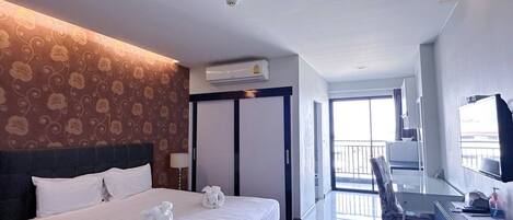 A hotel room with a bed, a desk, and a chair. There is a window and a door leading to a balcony.