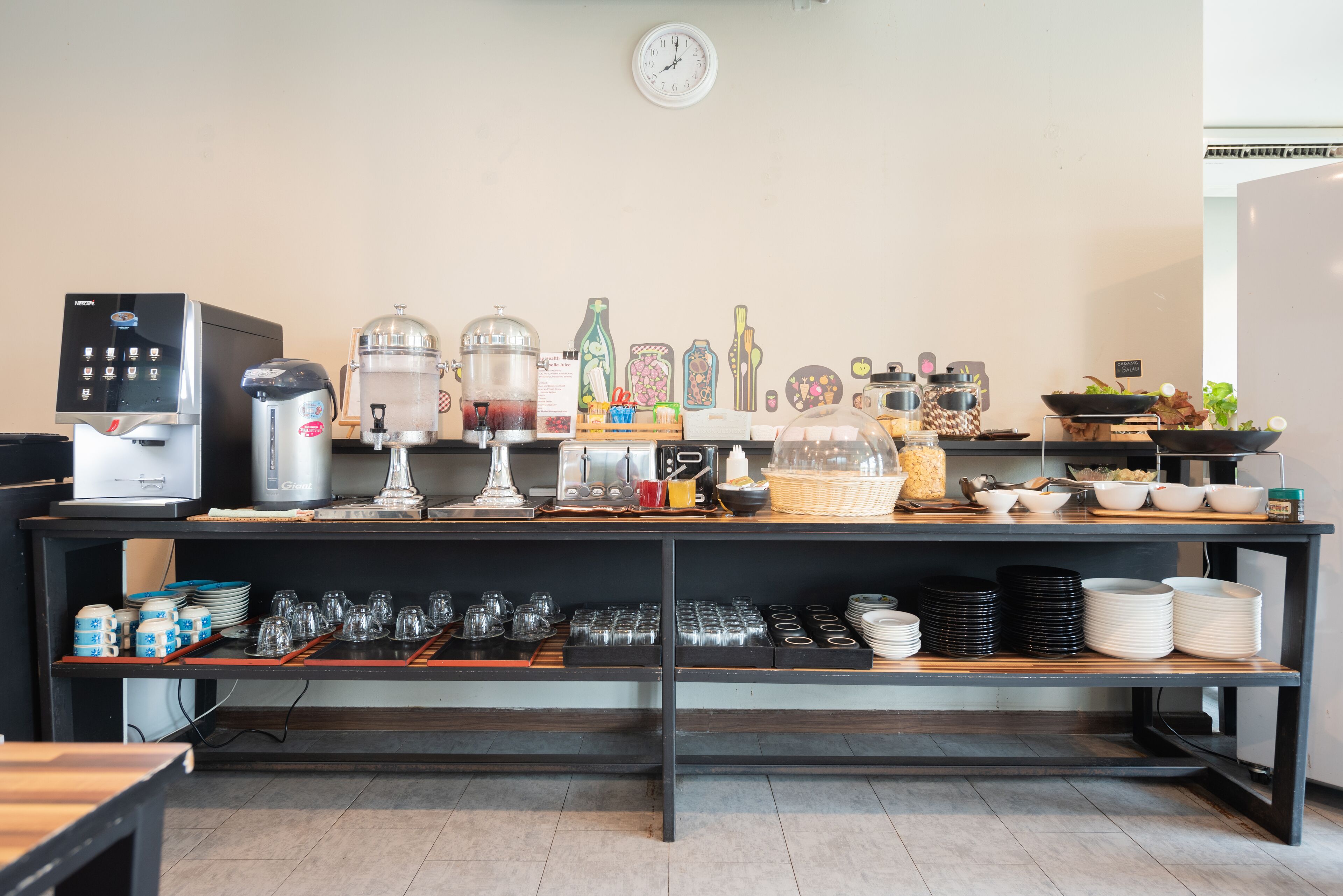 Una mesa de buffet con una máquina de café, dispensadores de bebidas y diversos alimentos a la vista.