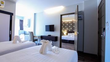 Habitación de hotel con dos camas, un escritorio, una silla, un televisor y un baño visible a través de una puerta abierta.
