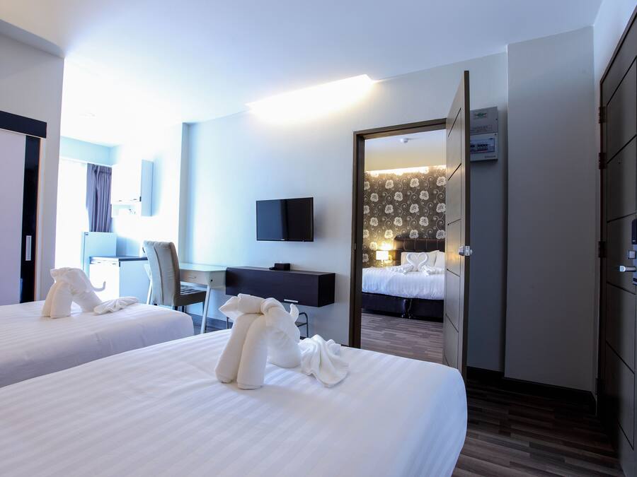 Habitación de hotel con dos camas, un escritorio, una silla, un televisor y un baño visible a través de una puerta abierta.