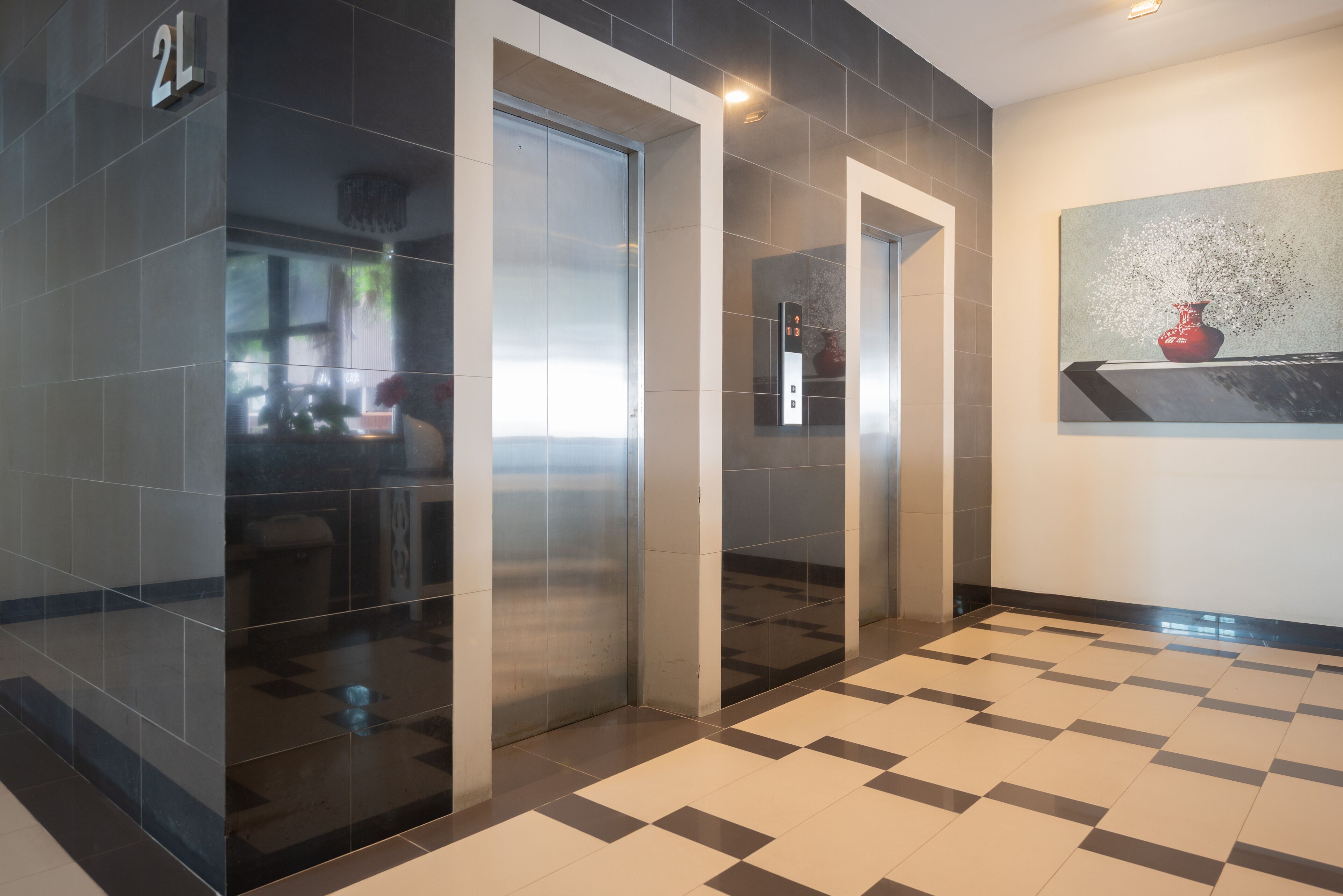 A modern elevator area with a checkered floor pattern, a visible elevator control panel, and a wall-mounted artwork.