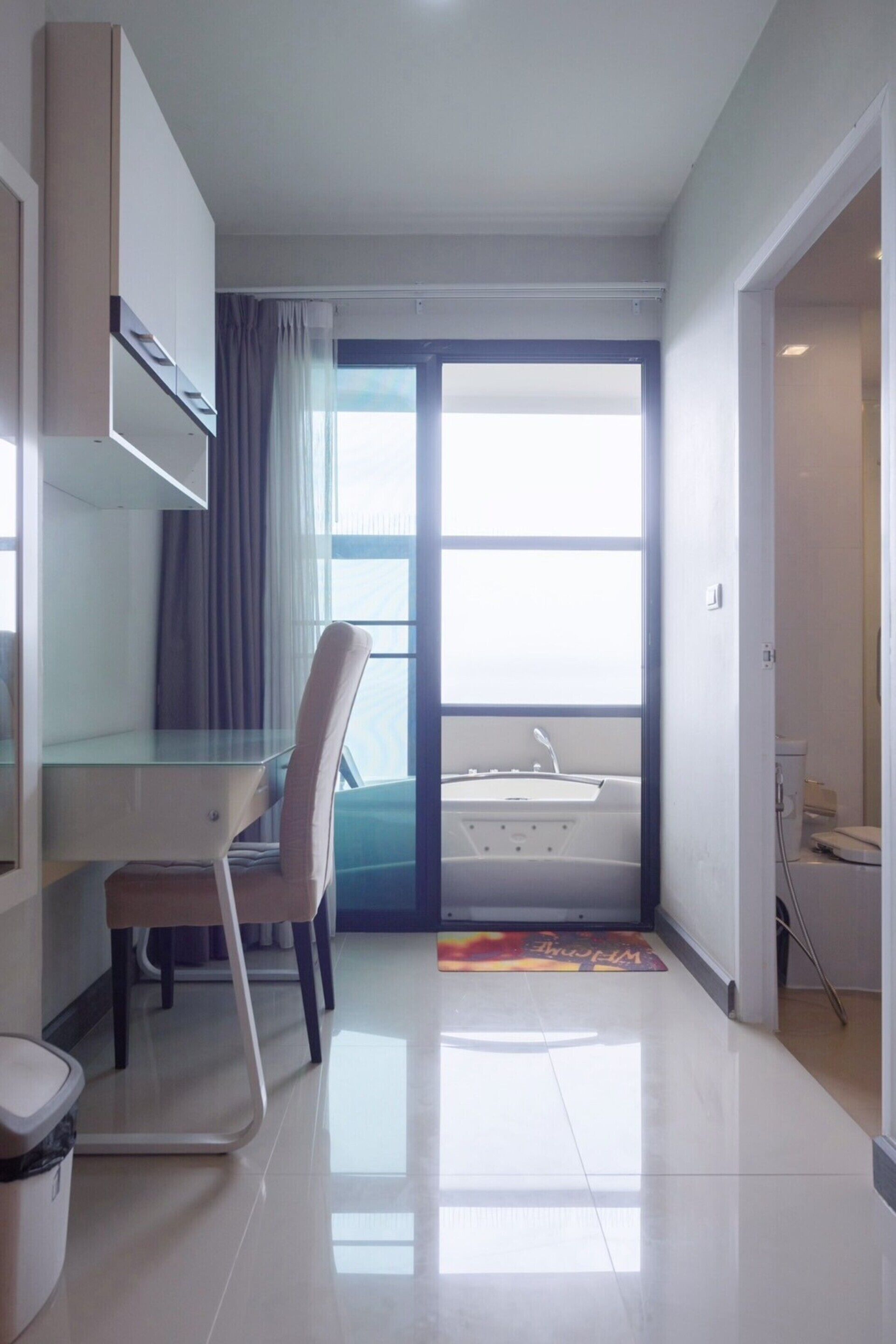 A modern hotel room with a glass desk, a chair, a small sink, and a view of the outside.