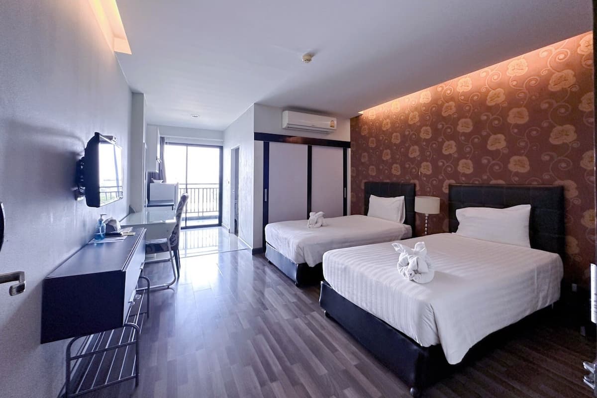 A hotel room with two beds, a desk, a chair, and a large window.