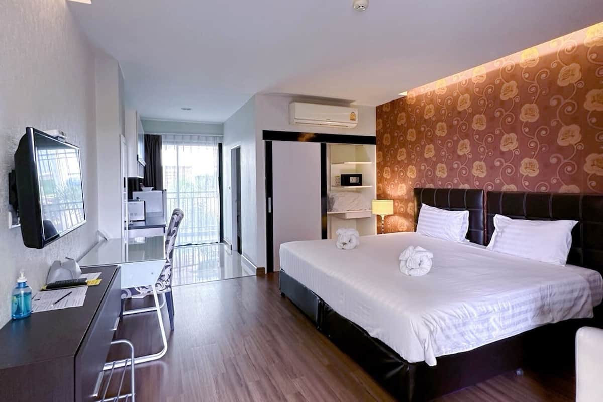 A hotel room with a bed, desk, chair, TV, and a view of the city.