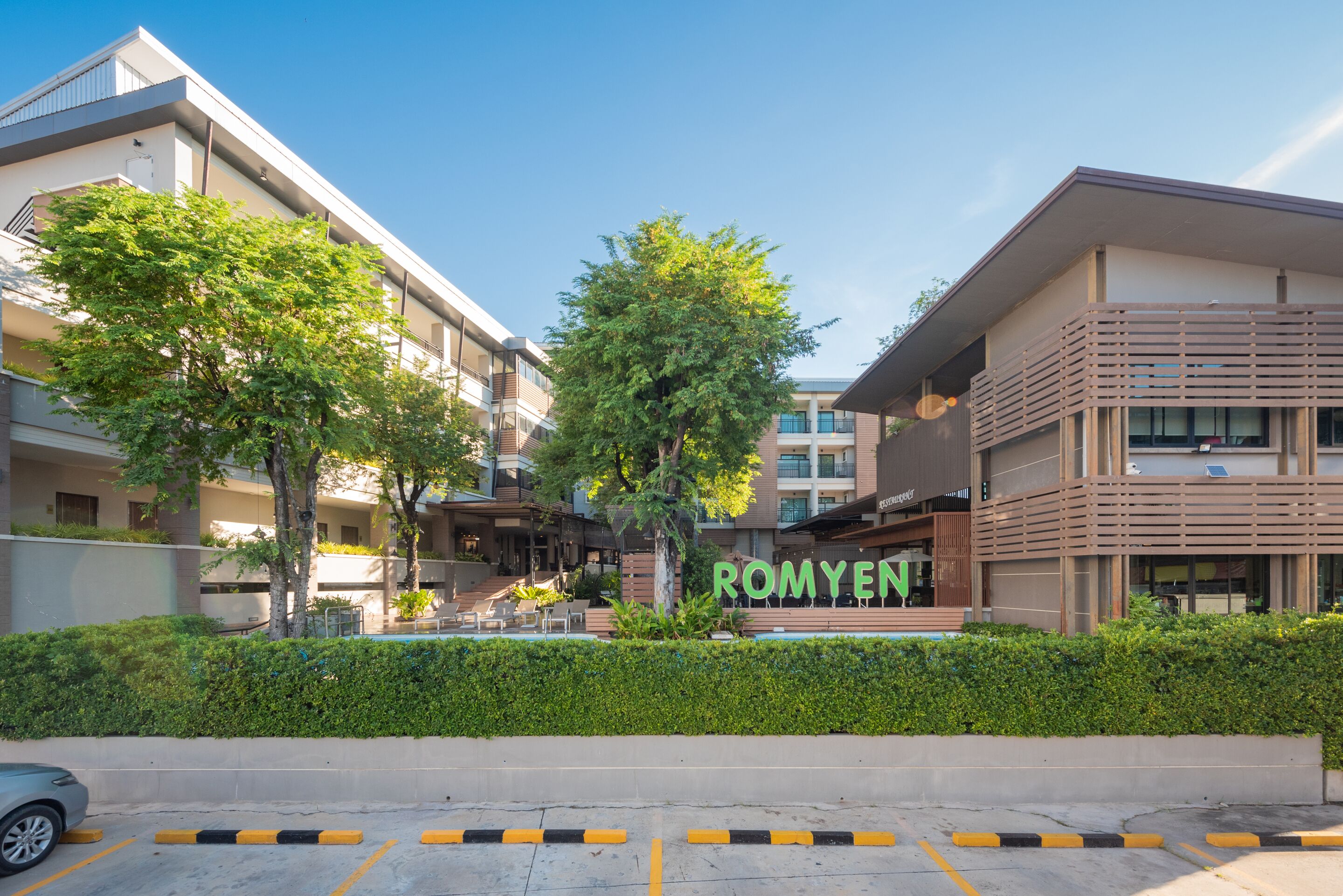 A modern building with a sign reading "ROMYEN" and a parking area with yellow and black striped barriers.