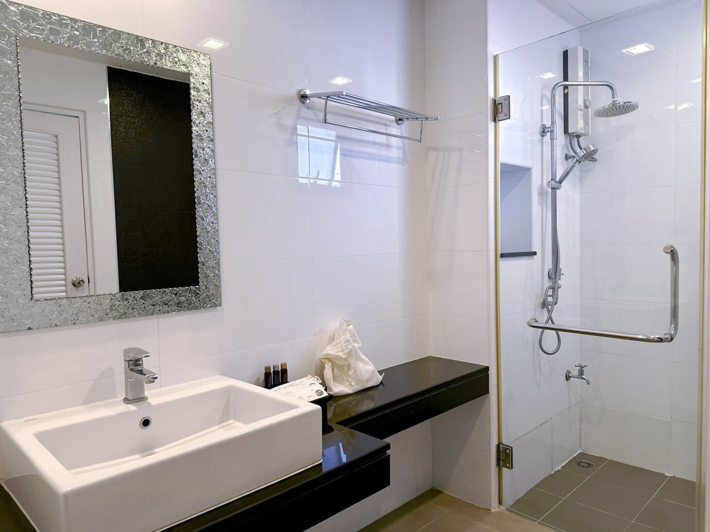 Un baño moderno con un lavamanos blanco, un espejo grande y una ducha a ras de suelo con cabezal de ducha de mano.
