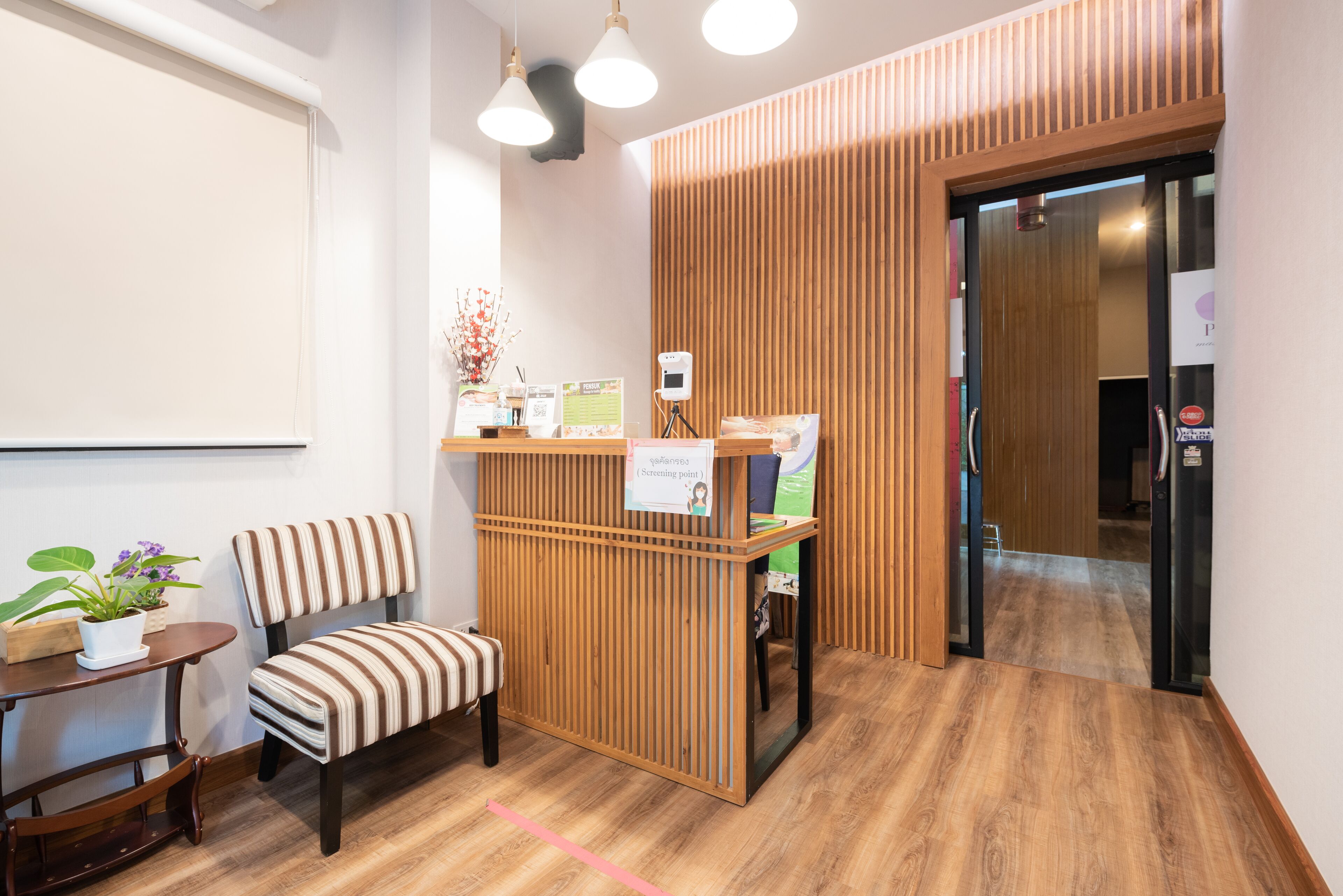 A reception area with a wooden desk, a striped chair, a small table with a potted plant, and a sign indicating a screening point.