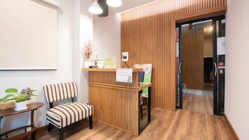 A reception area with a wooden desk, a striped chair, a small table with a potted plant, and a sign indicating a screening point.