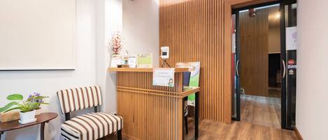 Un área de recepción con un mostrador de madera, una silla a rayas, una pequeña mesa con una planta en maceta y un cartel que indica un punto de control.