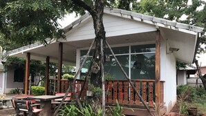 A covered outdoor seating area with a wooden bench and table, surrounded by potted plants and a tree. - Baan Ruankaew Resort (Nakhon Ratchasima)