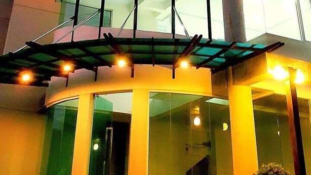 Un edificio moderno con fachada de vidrio curva, una destacada torre cilíndrica y una terraza en la azotea con iluminación.