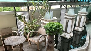 Una terraza de madera con una pequeña mesa y dos sillas, una planta en maceta y una fuente decorativa.