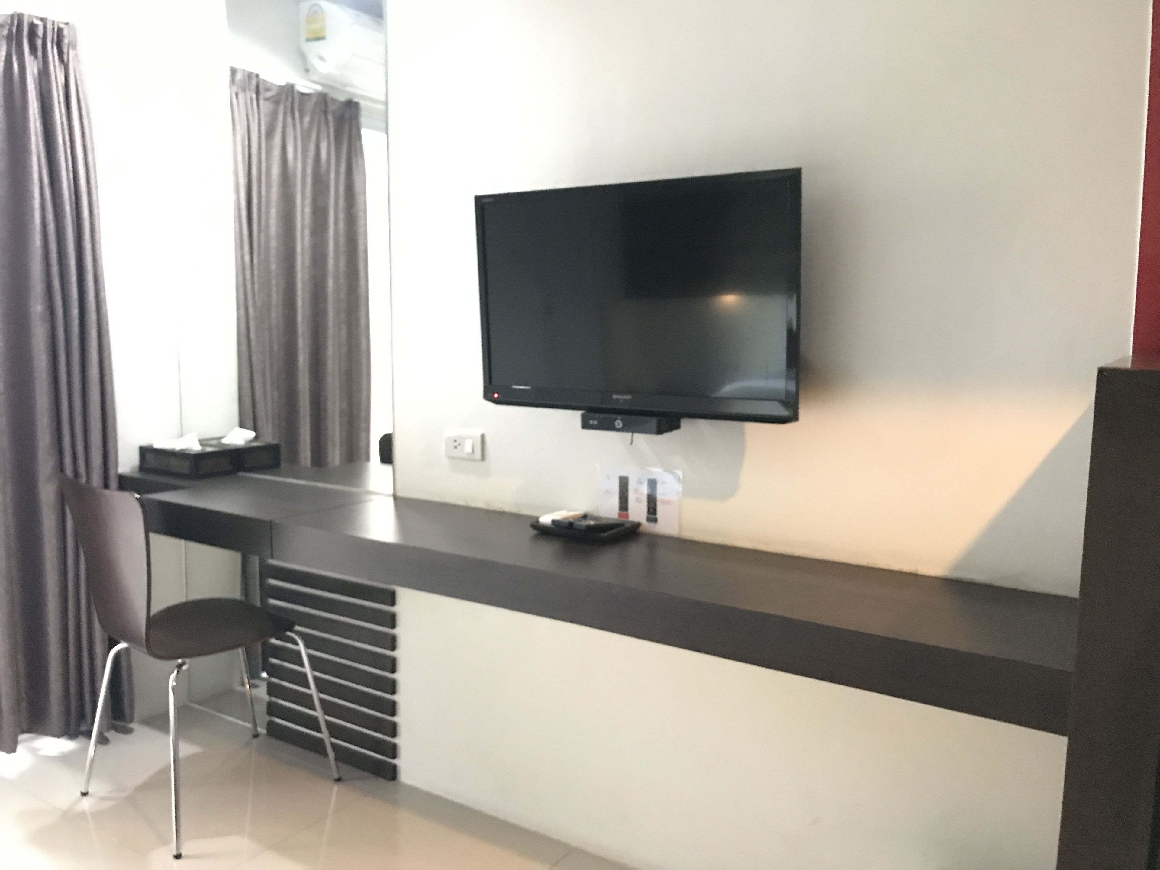 A modern room with a flat-screen TV mounted on a dark counter, a chair, and a small table with a remote control.